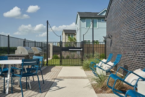 A patio with blue chairs and a table is surrounded by a black fence.