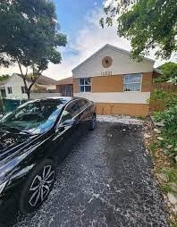 A black car is parked on a driveway in front of a house.
