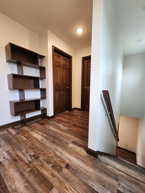 a living room with a wooden floor and a hallway with wooden shelves