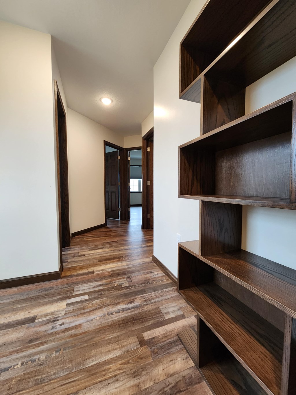 a corridor with wood floors and white walls and wooden shelves
