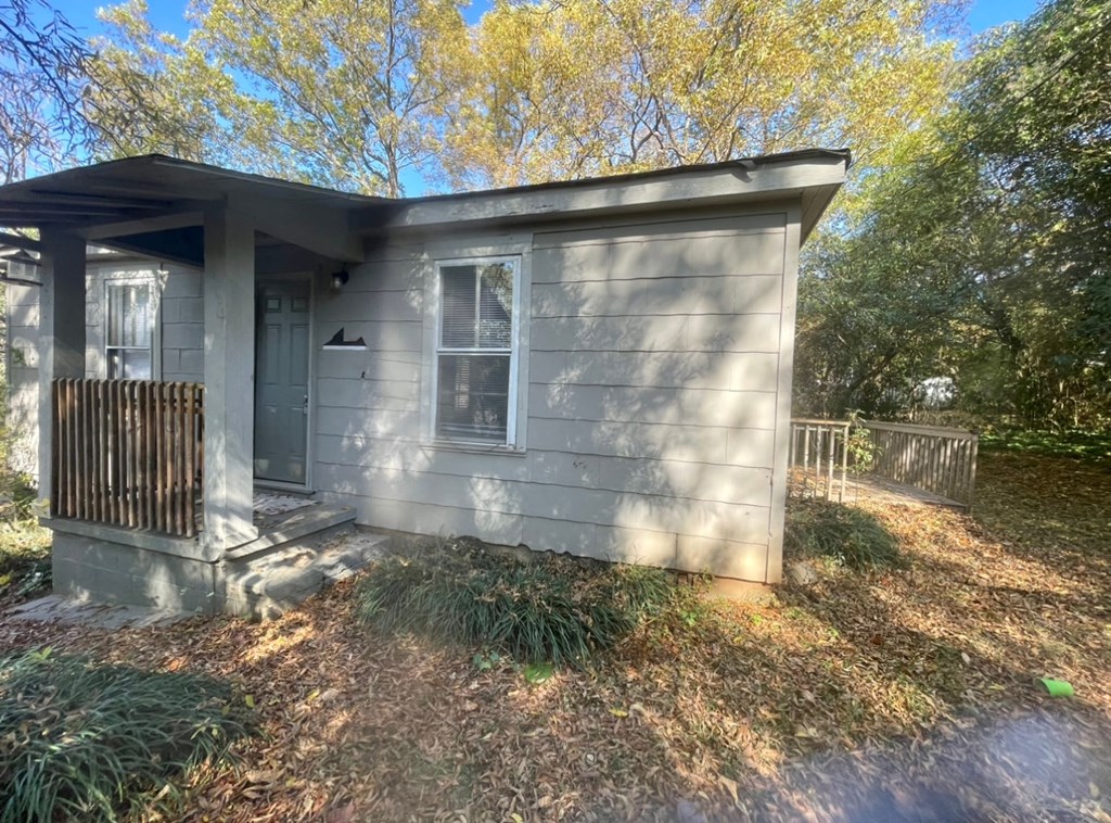 the front of a small gray house with a fence and trees