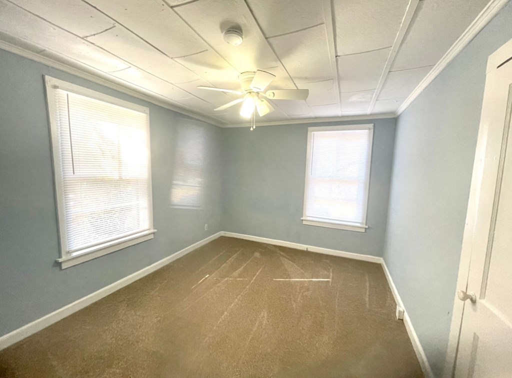 an empty room with a ceiling fan and two windows