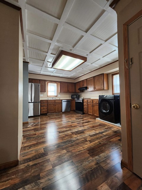 an empty kitchen with wooden floors and cabinets and a window
