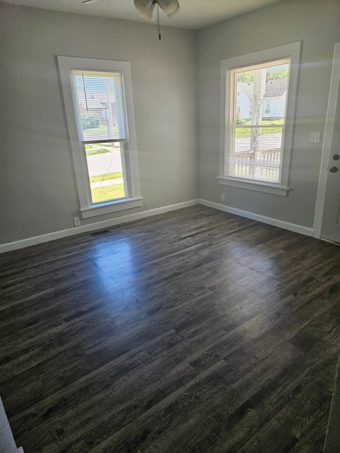 an empty living room with wooden floors and two windows