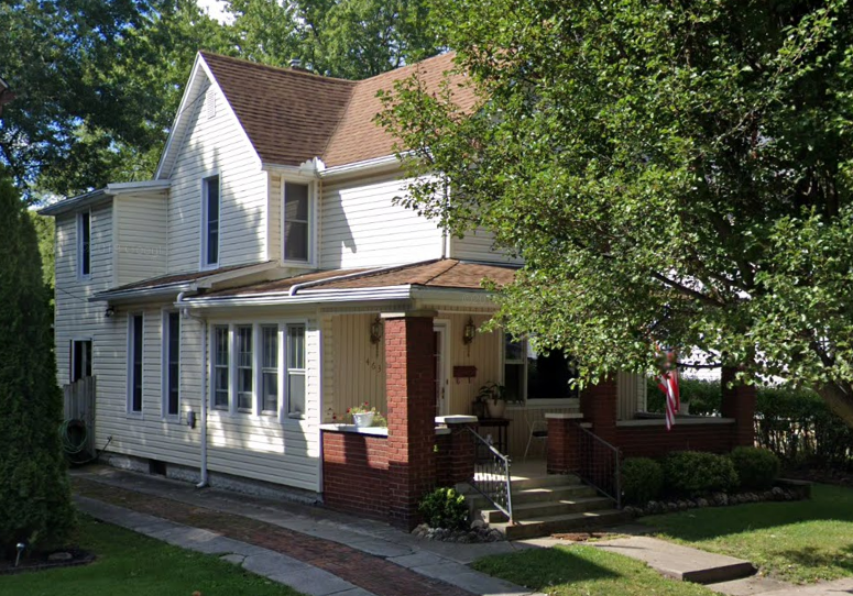 a white house with a porch and a tree