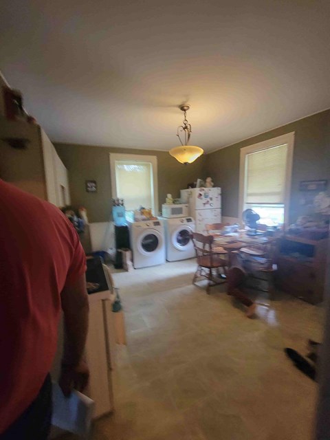 A man in a red shirt is standing in a kitchen with a washer and dryer.