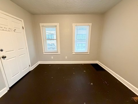 A room with a white door and two windows with white blinds.