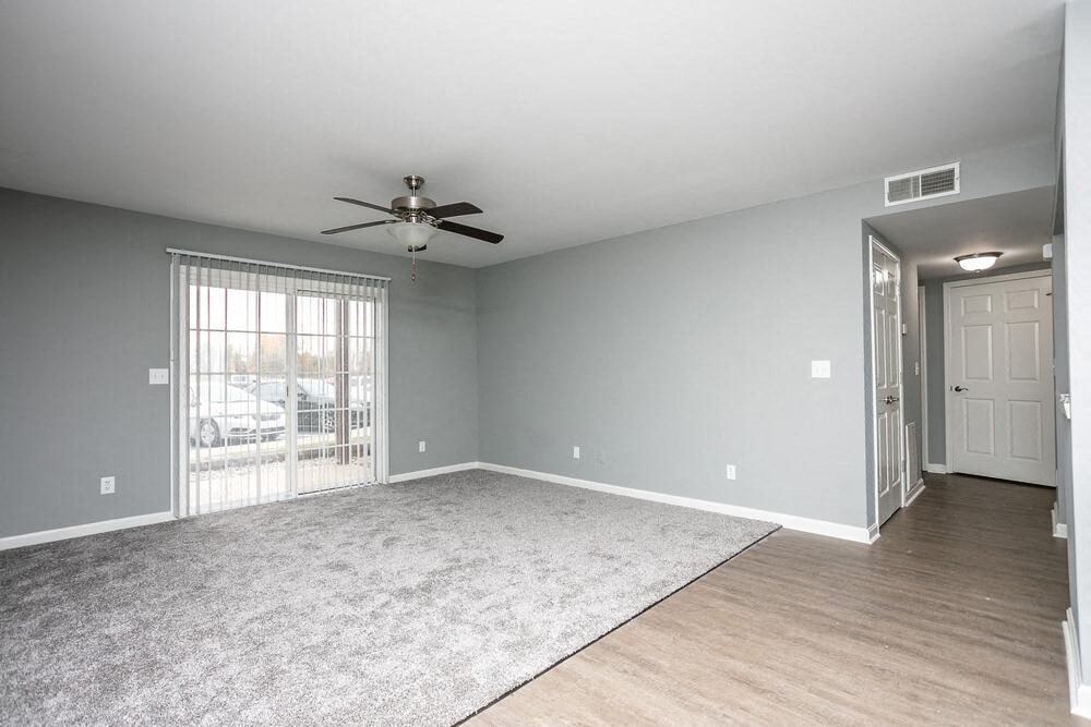A spacious room with a ceiling fan and sliding glass doors leading to a parking lot.