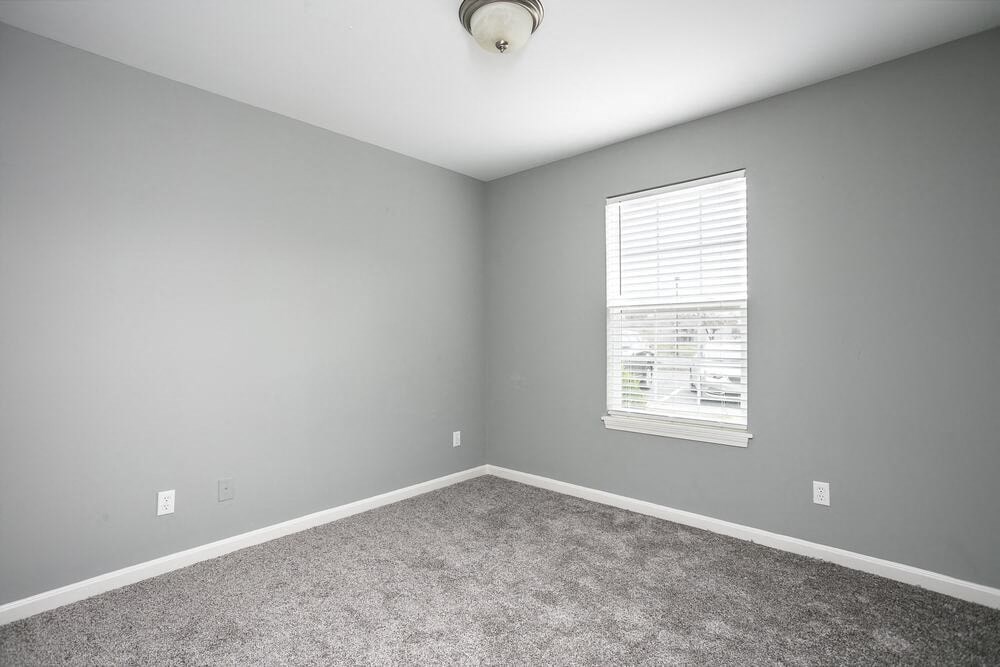 A room with a carpeted floor and a window with blinds.