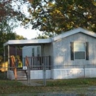 a small white house with a deck and a tree