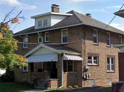 A two-story brick house with a white roof and a covered porch.
