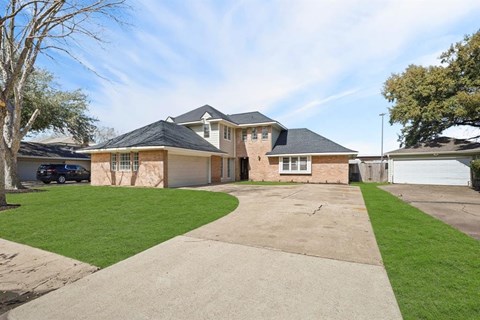the front of a brick house with a driveway and lawn