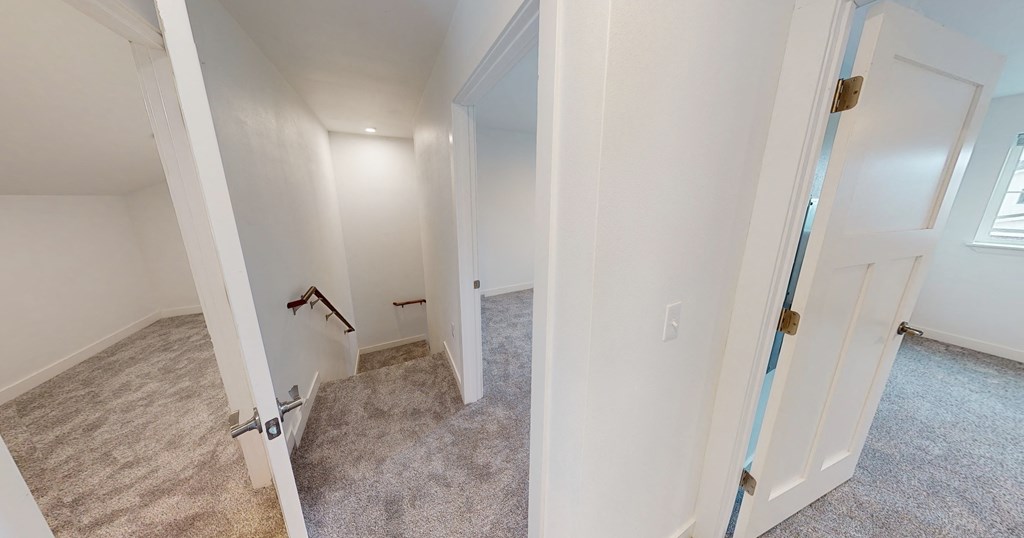 an empty bedroom and hallway with white walls and carpeted floors