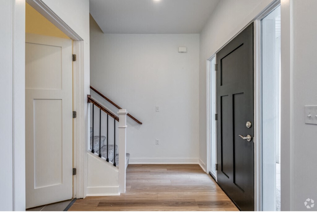an empty room with a black door and a hallway with wood floors and a staircase