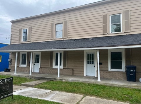 A two-story building with a porch and a sign that says "FOR RENT" in front of it.