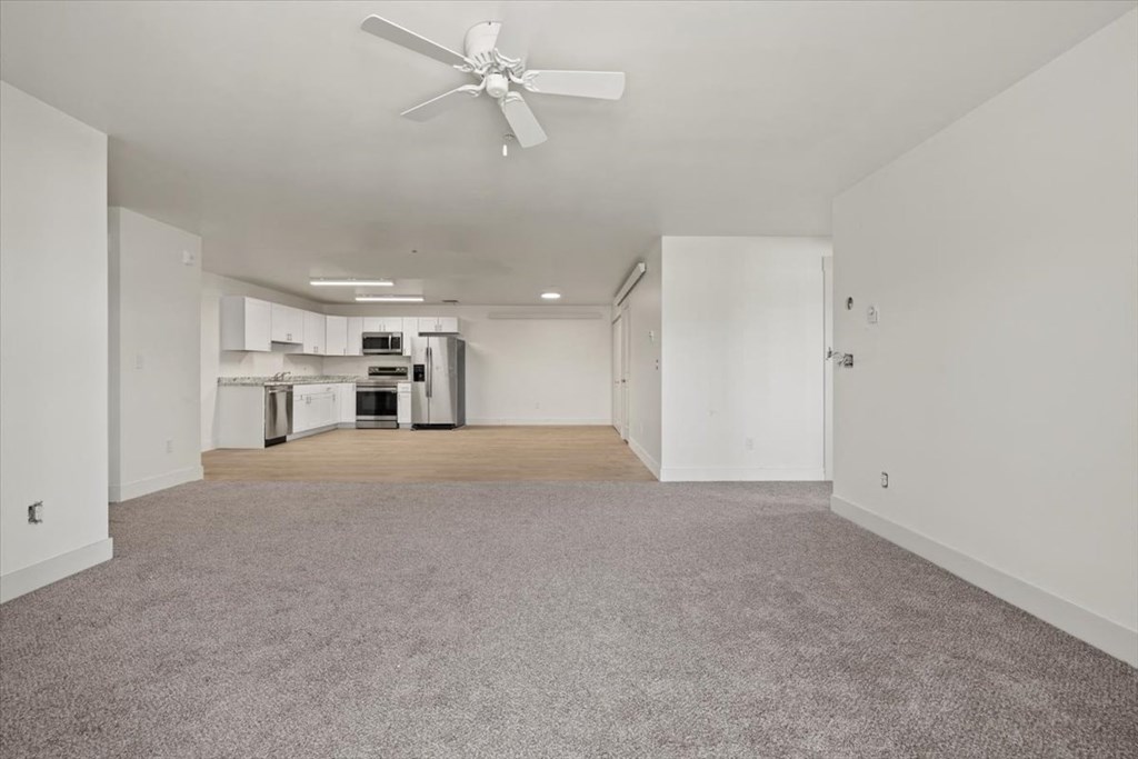 an empty living room and kitchen with a ceiling fan