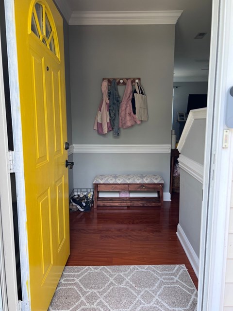 A yellow door is open to a hallway with a bench and coat rack.