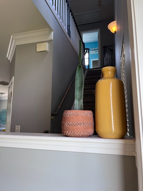 A yellow vase sits on a ledge next to a pink basket.