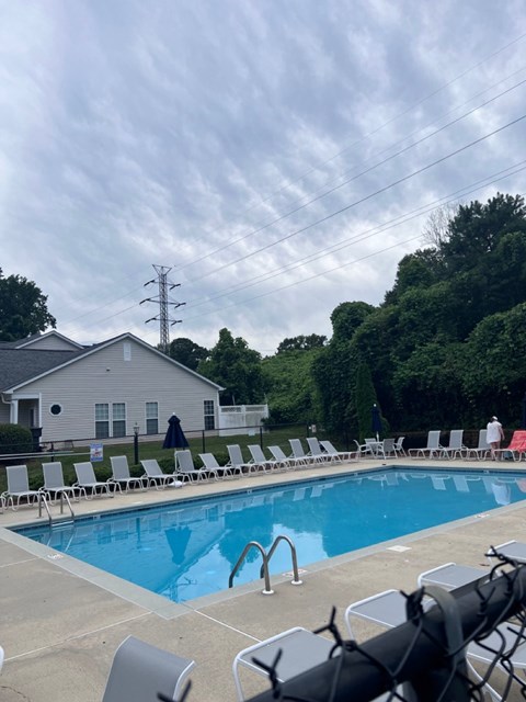 A pool with chairs around it and a house in the background.