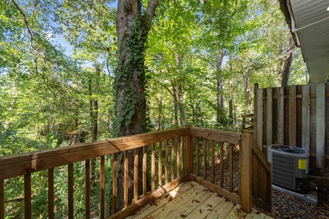 A wooden deck with a railing and a tree in the background.