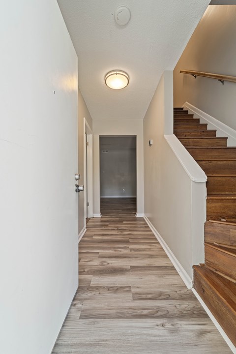 A hallway with wooden floors and a staircase on the right.