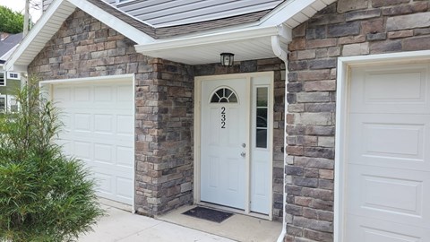 the front door of a brick house with two garage doors