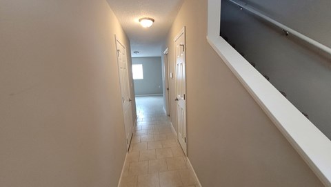a long hallway with a staircase and a door to a room with a door open