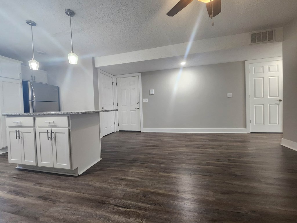 an empty living room with a kitchen and a ceiling fan