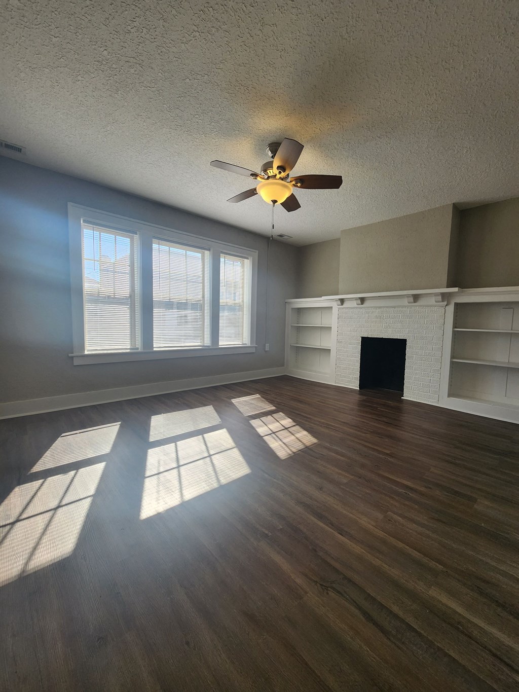 an empty living room with a ceiling fan and a fireplace