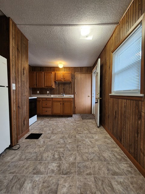an empty kitchen with wooden cabinets and a white refrigerator