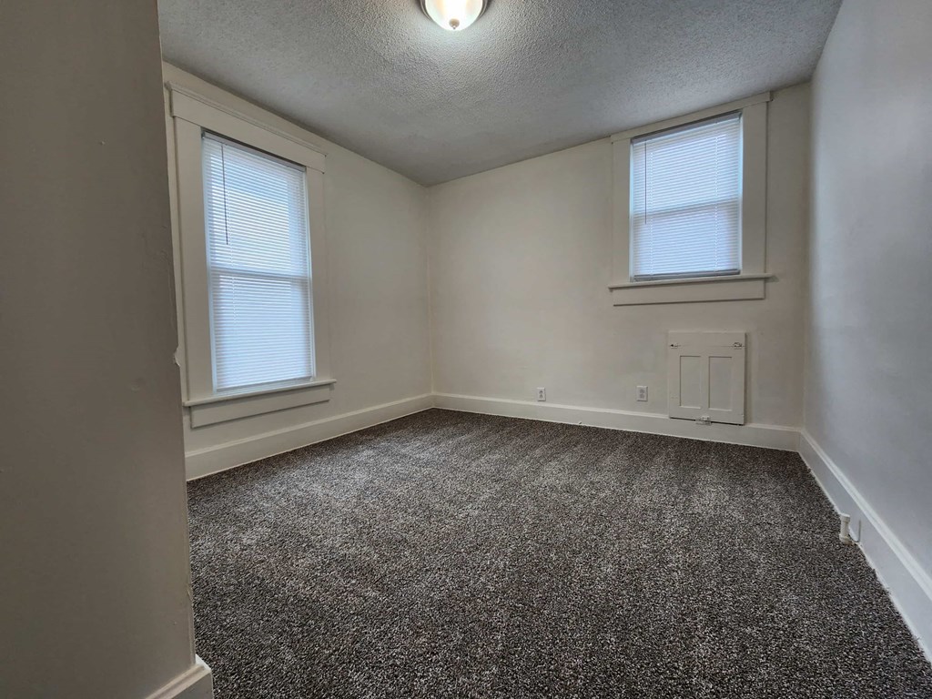 an empty bedroom with two windows and a carpeted floor