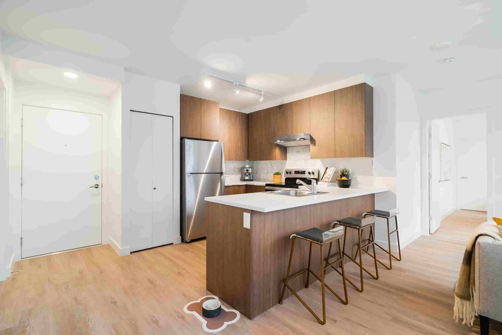 A kitchen with a refrigerator, stove, and bar stools.