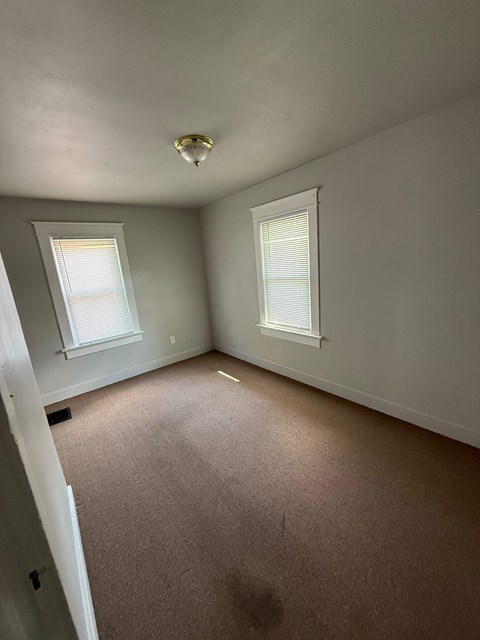 A room with carpeted floor and two windows.