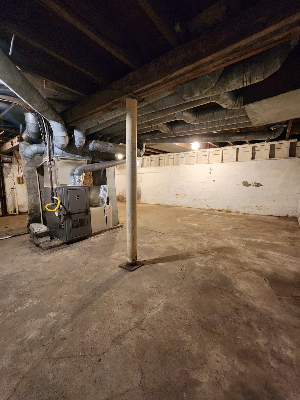 a large empty basement with a heater and a pole