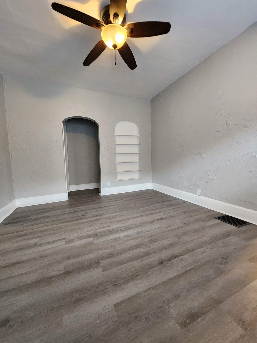 an empty living room with a ceiling fan and wood floors