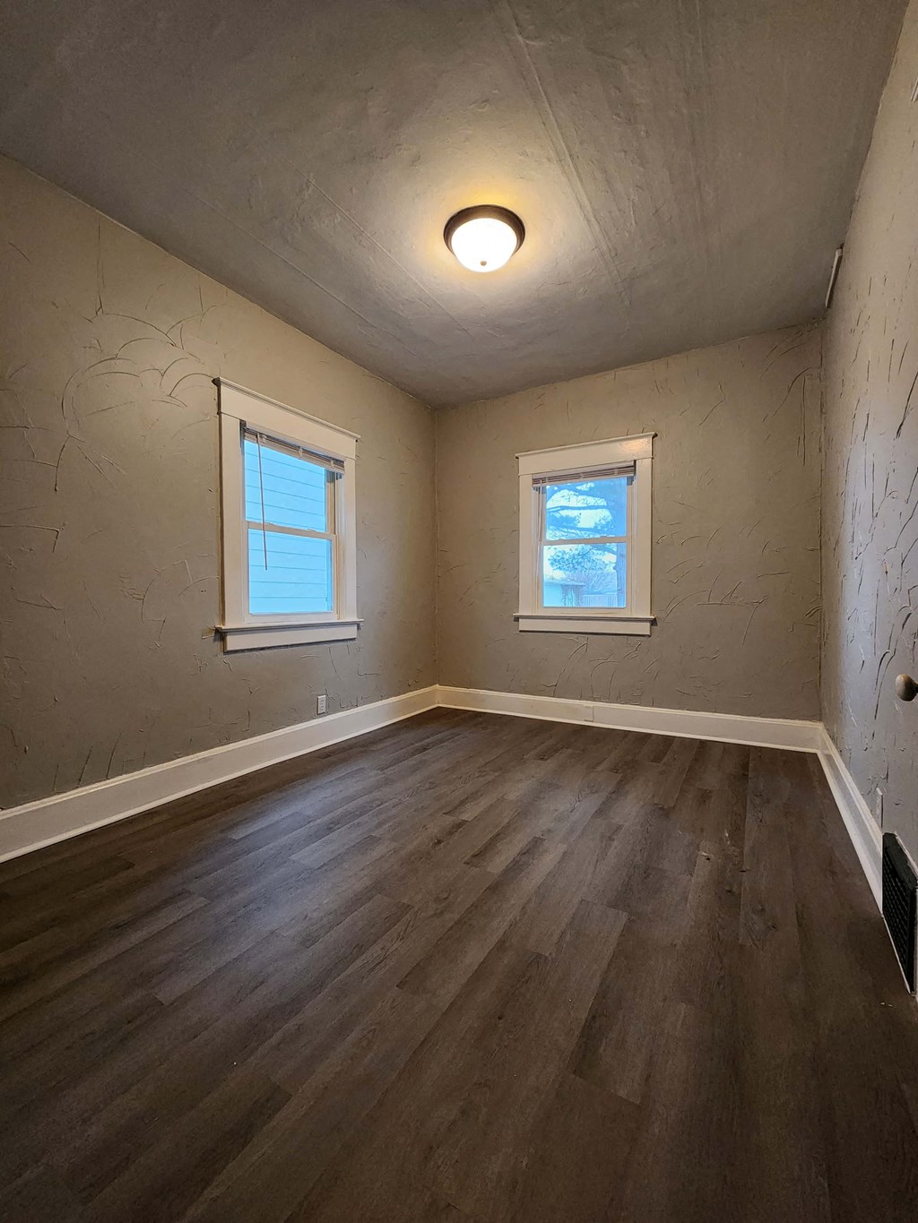 an empty room with wooden floors and two windows