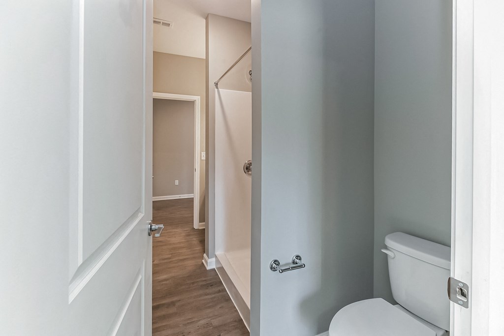 an empty bathroom with a toilet and a hallway with a door open to a closet