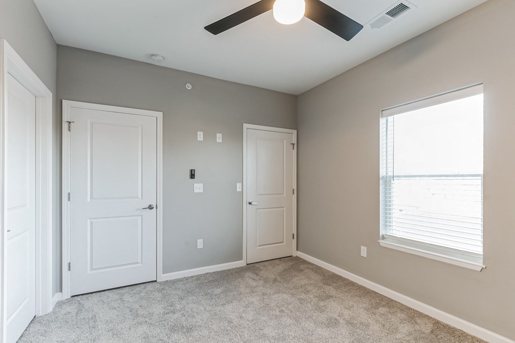 an empty bedroom with two doors and a ceiling fan