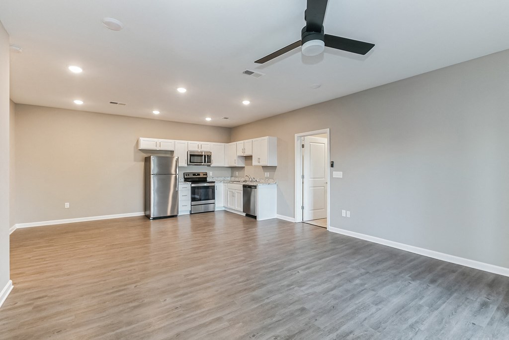 an empty living room with a kitchen and a ceiling fan