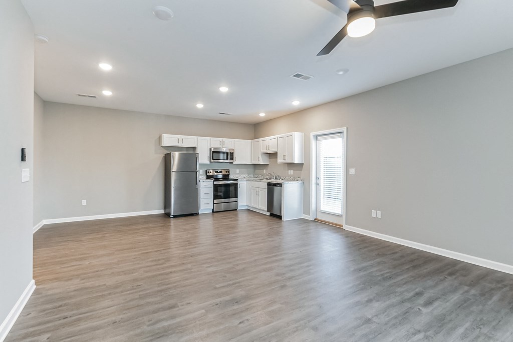 an empty living room with a kitchen and a ceiling fan