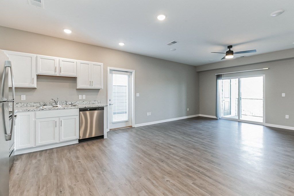 an empty living room and kitchen with white cabinets and stainless steel appliances