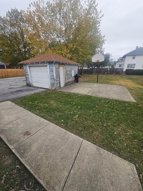 A basketball hoop stands in a backyard with a shed and a concrete walkway.