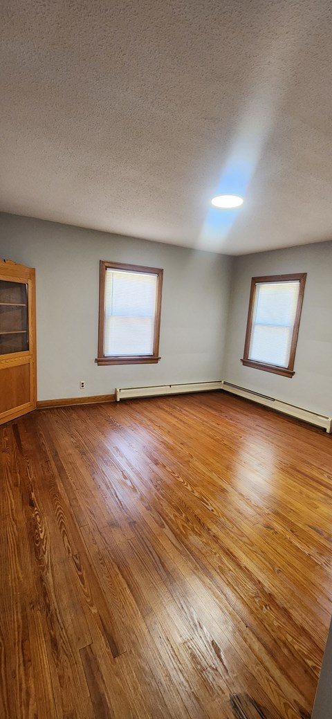 an empty living room with wooden floors and two windows