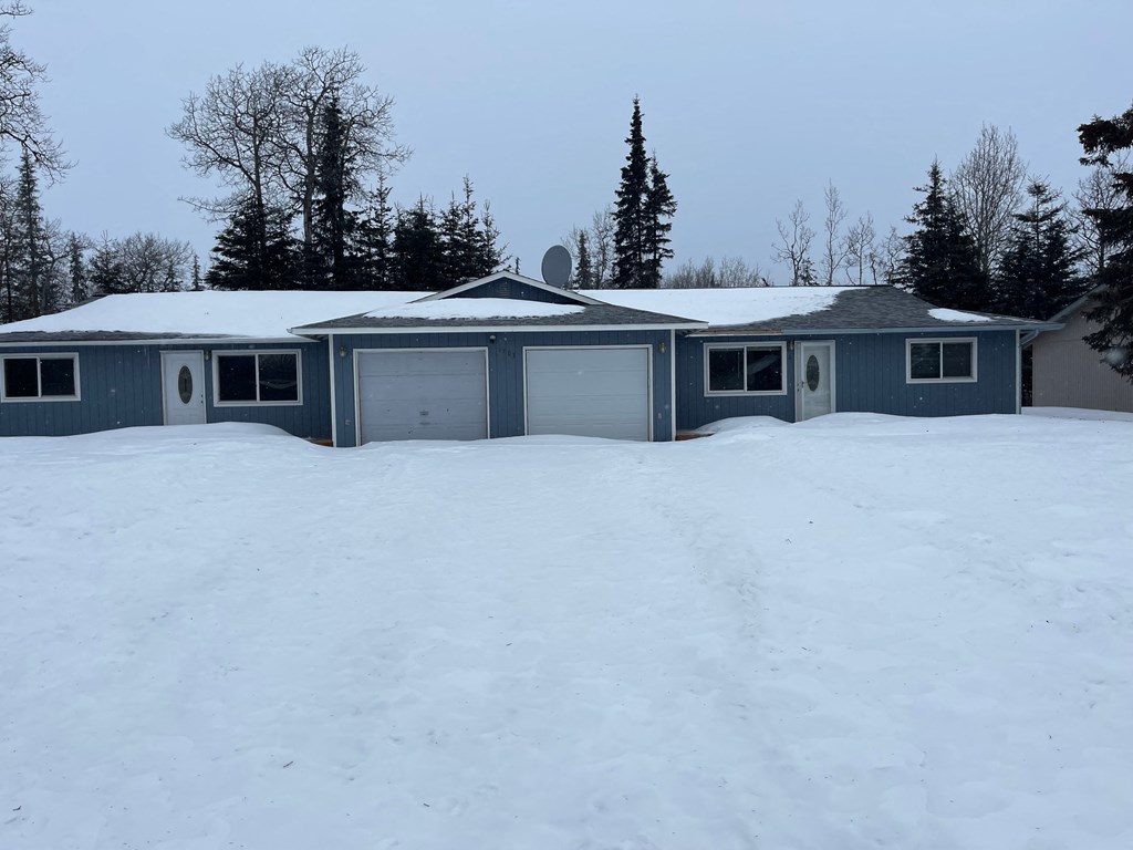 A house with a grey roof and a garage door is surrounded by snow.