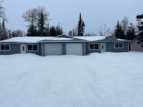A house with a grey roof and a garage door is surrounded by snow.