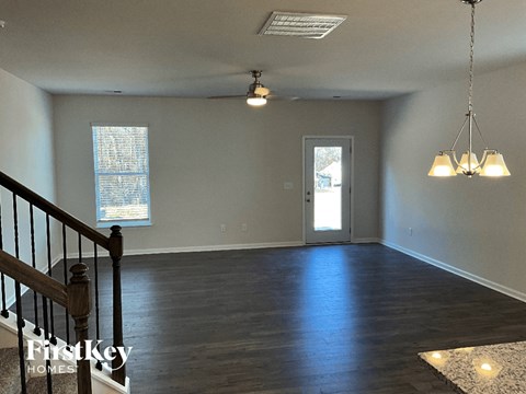 an empty living room with a staircase and a door to the kitchen