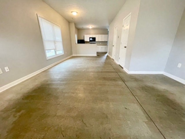 an empty living room with a cement floor and a kitchen