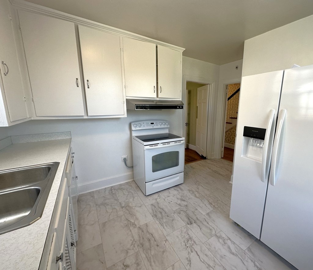 an empty kitchen with white cabinets and a stove and refrigerator