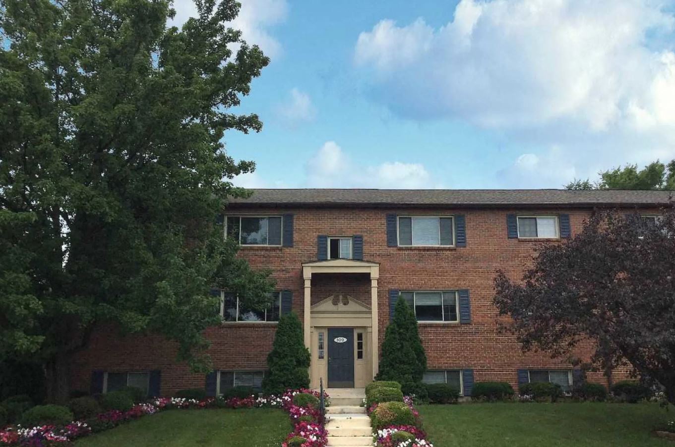 the front of a brick apartment building with a blue sky and some flowers