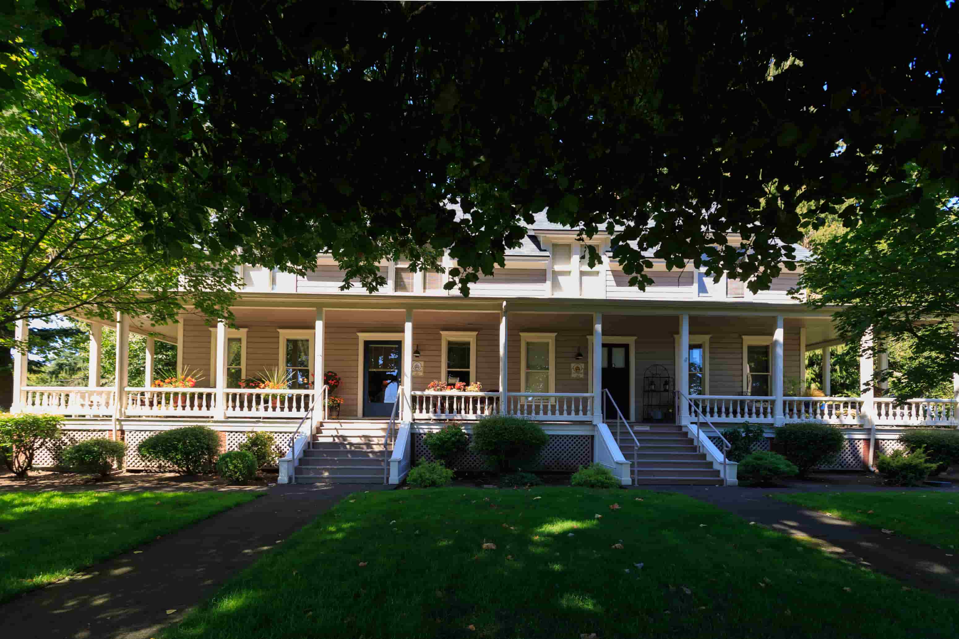 A white house with a porch and a tree in front.